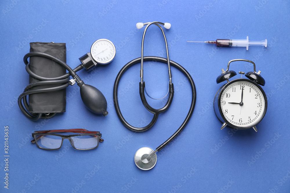 Stethoscope with sphygmomanometer, syringe, alarm clock and eyeglasses on color background Stethoscope with sphygmomanometer, syringe, alarm clock and eyeglasses on color background