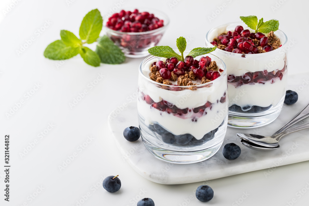 A close up view of two pomegranate and blueberry yogurt parfaits with a small bowl of pomegranate arils in behind. A close up view of two pomegranate and blueberry yogurt parfaits with a small bowl of pomegranate arils in behind.