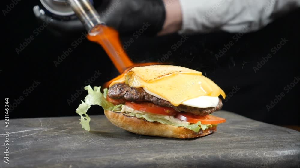 Chef using blow torch to burn cheese on tasty burger. Cook Melting