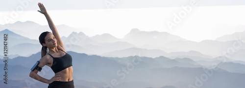 A thin athletic girl takes a break between classes on the background of mountains in the early morning, enjoys silence and freedom.