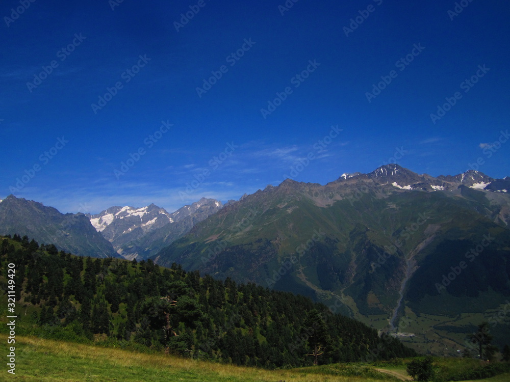 Mountain landscape of Svaneti on bright summer sunny day. Mountain lake, hills covered green grass on snowy rocky mountains background. Caucasus peaks in Georgia. Amazing view on wild georgian nature