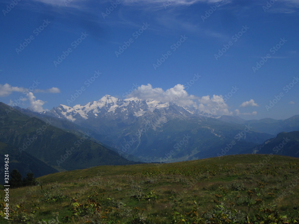 Naklejka premium Mountain landscape of Svaneti on bright summer sunny day. Mountain lake, hills covered green grass on snowy rocky mountains background. Caucasus peaks in Georgia. Amazing view on wild georgian nature