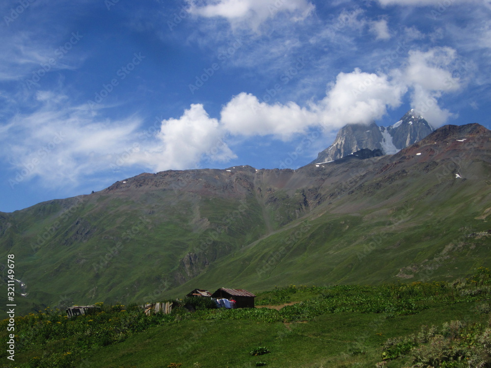 Mountain landscape of Svaneti on bright summer sunny day. Mountain lake, hills covered green grass on snowy rocky mountains background. Caucasus peaks in Georgia. Amazing view on wild georgian nature