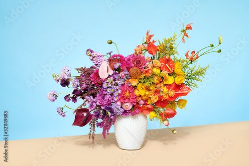 Contemporary Floral Arrangement with Anthurium Dahlia flowers in vase on table top with solid colors