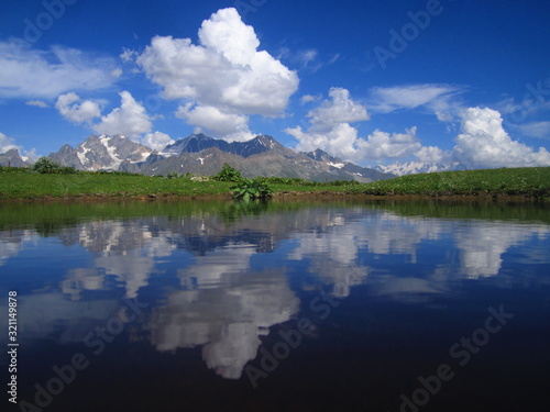 Mountain landscape of Svaneti on bright summer sunny day. Mountain lake, hills covered green grass on snowy rocky mountains background. Caucasus peaks in Georgia. Amazing view on wild georgian nature