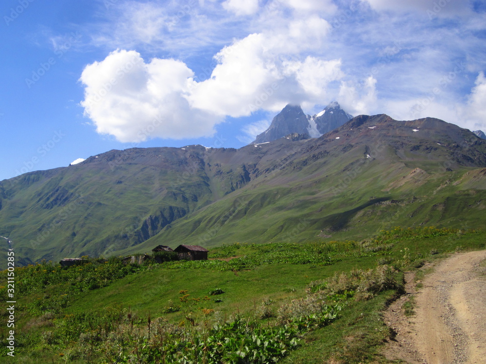 Mountain landscape of Svaneti on bright summer sunny day. Mountain lake, hills covered green grass on snowy rocky mountains background. Caucasus peaks in Georgia. Amazing view on wild georgian nature Mountain landscape of Svaneti on bright summer sunny day. Mountain lake, hills covered green grass on snowy rocky mountains background. Caucasus peaks in Georgia. Amazing view on wild georgian nature