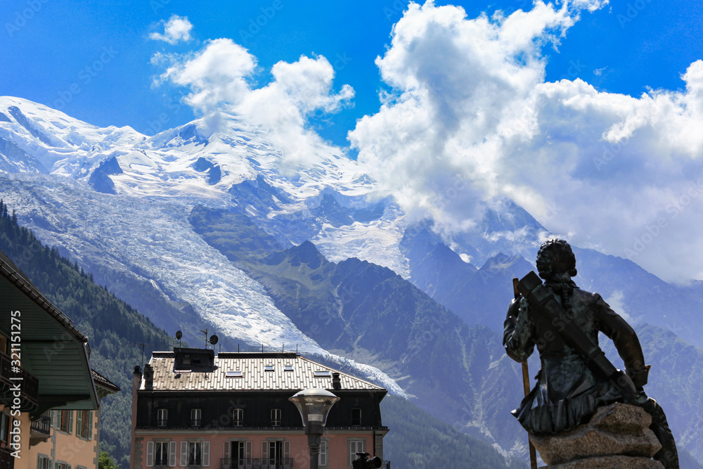 Stunning view of Mont Blanc, highest peak of Alps, from Chamonix in summer sunny day, blue sky cloud in background, statue of Michel Gabriel Paccard, first ascent, Monument in foreground, France