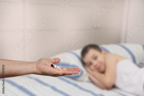 female hand holds out  offering  a handful of colored pills and capsules  close-up  blurred image of a lying child in the background  copy space  concept of medical care  treatment