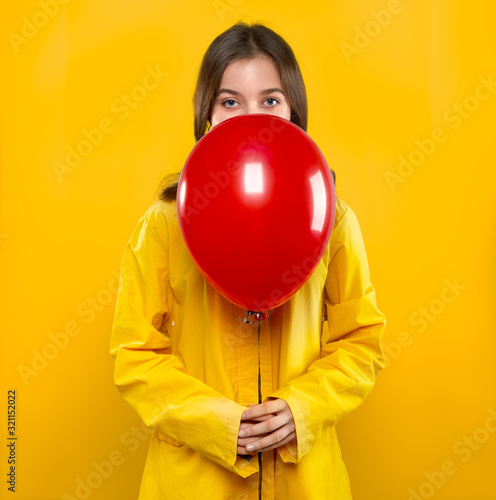Pretty girl teenager in yellow coat with red air balloon in hands on yellow background. Concept to Valentines day holiday. Studio portrait. © LoopAll
