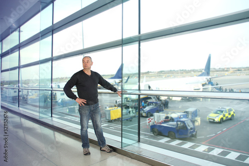 man, a passenger, waiting for his flight, stands at the window and looks at the airport runway, a travel concert