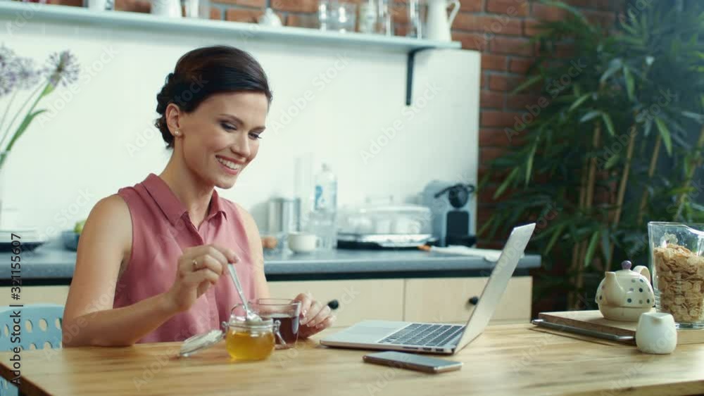 Woman using laptop for video call online. Girl pouring honey into cup of tea. Woman using laptop for video call online. Girl pouring honey into cup of tea.