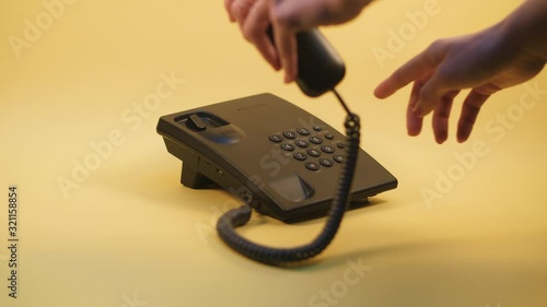 woman s hand picks up the phone dials the number and then hangs up from the old push-button office phone on a yellow background