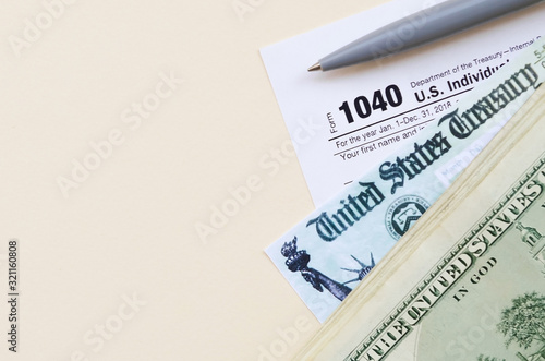 1040 Individual Income tax return form with Refund Check and hundred dollar bills on beige background photo