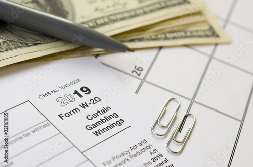 IRS Form W-2G Certain Gambling Winning blank lies with pen and many hundred dollar bills on calendar page photo