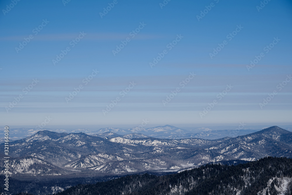 Winter mountain landscape. Snow-capped mountains overgrown with taiga against a blue sky. Russia. Altai Republic.