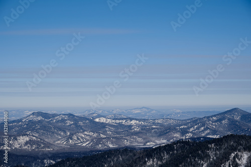 Winter mountain landscape. Snow-capped mountains overgrown with taiga against a blue sky. Russia. Altai Republic.