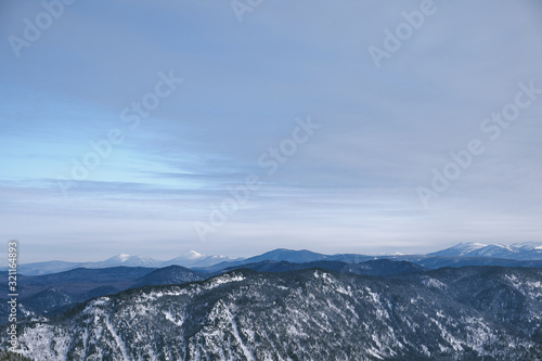 Winter mountain landscape.Snow mountains overgrown with taiga against a blue sky. Top view. Russia. Altai Republic.