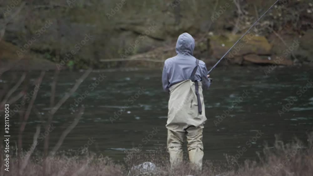Male in waders alone fishing casting lure splashing on river water bank on sandy river in pacific northwest oregon in slow motion Male in waders alone fishing casting lure splashing on river water bank on sandy river in pacific northwest oregon in slow motion