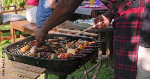 Black man grilling barbecue during party. Multi ethic friends party, garden, outdoor, vintage look. Spring, summer vibe concept.