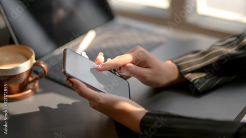 Cropped shot of businesswomen texting on blank screen smartphone in modern dark office room