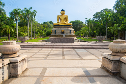 An iconic golden Buddha statue in Viharamahadevi Park a public park located in Colombo, Sri Lanka. Viharamahadevi park is the oldest and largest park of the Port of Colombo. photo