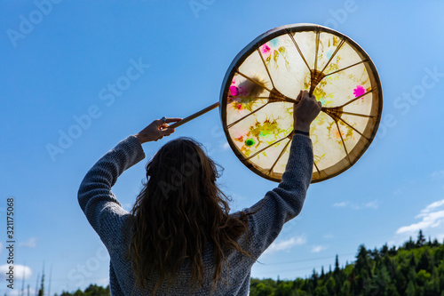 Rear closeup view of young shamanic woman holding sacred native frame drum with raised hands worshiping in Northern Quebec in Canada