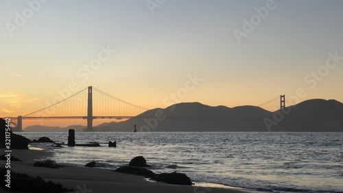 Light waves crashing on calm beach at sunset with Golden Gate Bridge photo