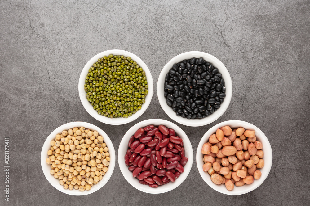 Grains or beans, red bean, black bean, green bean, soybean, peanut in the white bowl placed on the black cement floor. Top view.