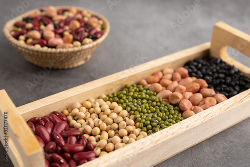 Grains or beans, red bean, black bean, green bean, soybean, peanut in the wooden tray and the wooden basket placed on the black cement floor. High angle view. © pon301229