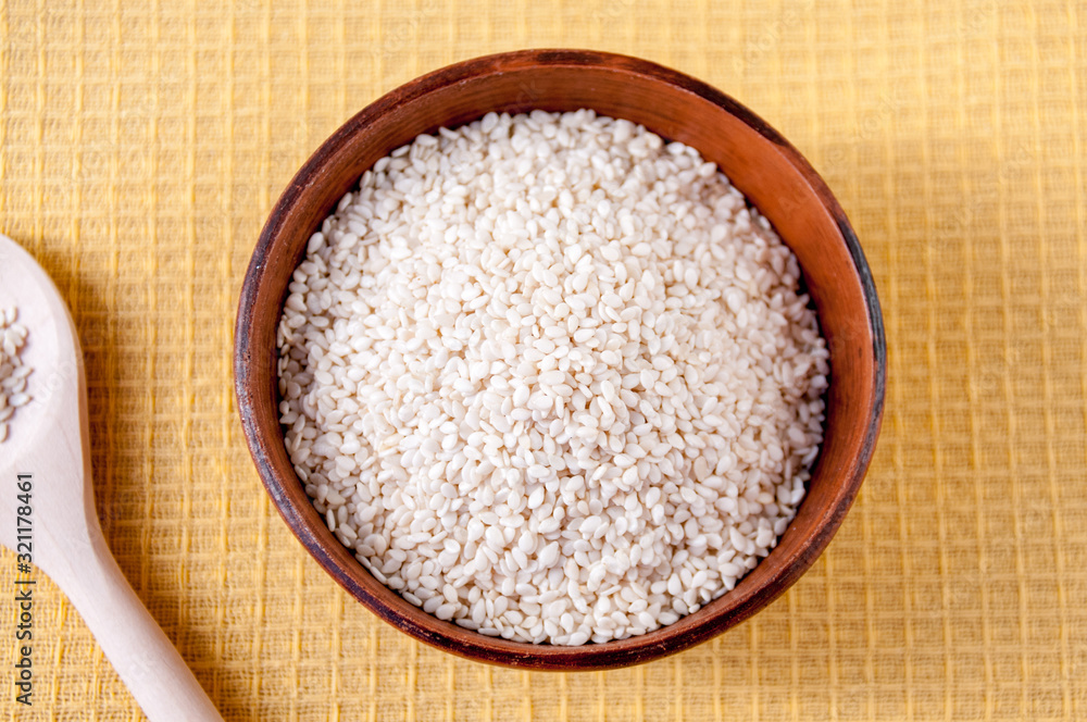 White sesame seeds in a clay Cup and wooden spoon on the table, top view White sesame seeds in a clay Cup and wooden spoon on the table, top view