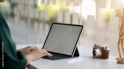 Cropped shot of female designer typing on blank screen tablet in simple co working space
