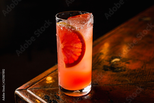 An orange low ABV cocktail in a highball glass filled with ice and garnished with a piece of orange