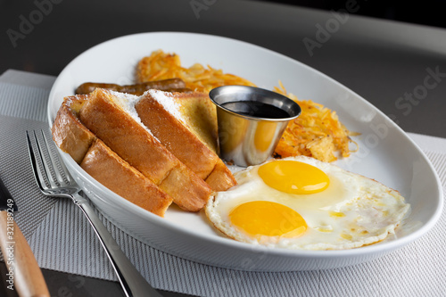 Obraz na płótnie A view of a breakfast plate in a restaurant or kitchen setting, featuring hash browns, sausage links and French toast