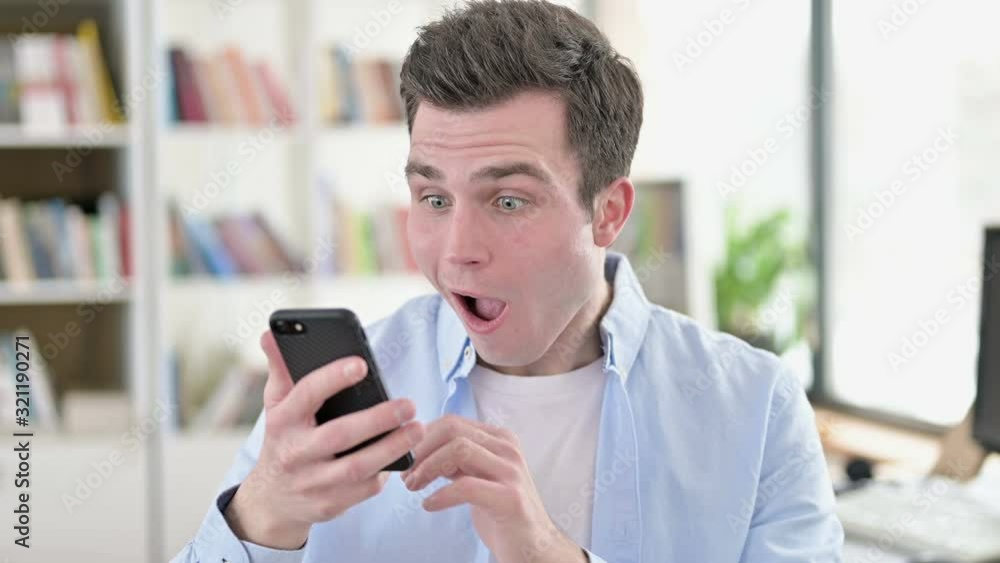 Young Man Celebrating Success on Smartphone Young Man Celebrating Success on Smartphone