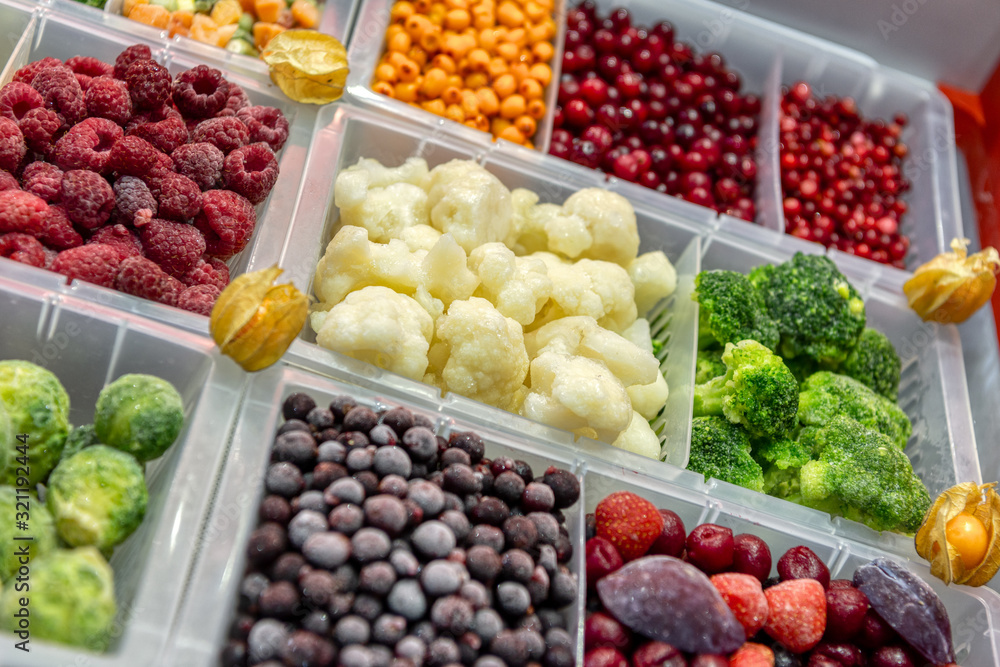 Frozen vegetables, fruits and berries are in plastic boxes. In the center of the frame is cauliflower.