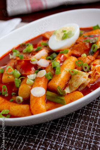 A view of a plate of Korean Tteok-bokki, which is a spicy rice cake dish, in a restaurant or kitchen setting.