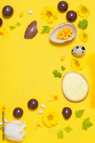 Easter yellow background with chocolatte eggs, candy and spri