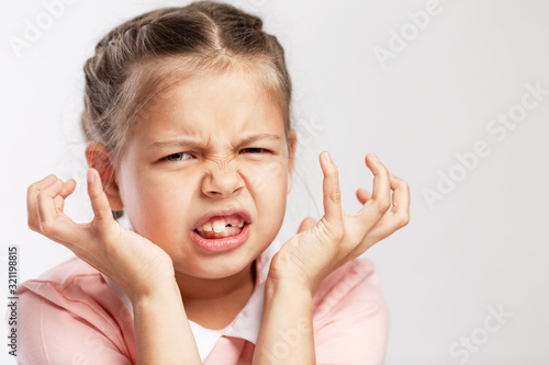 The school-age girl in a pink sweater is angry. White background. Close-up.