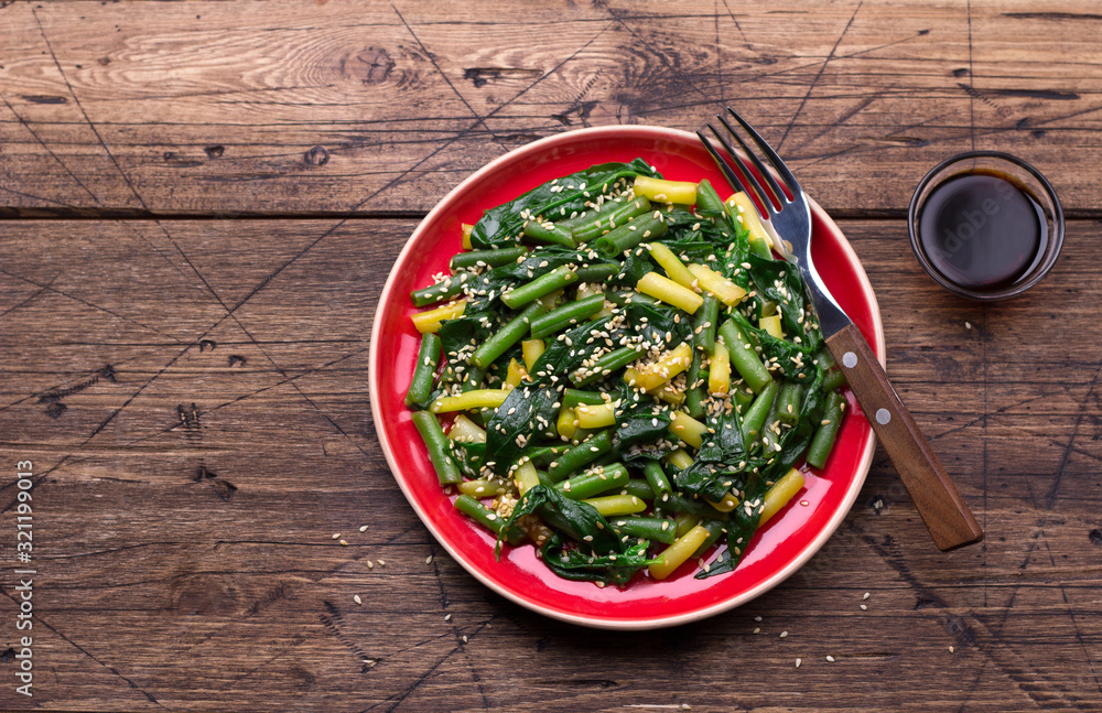 Green and yellow beans with spinach, sesame seeds and soy sauce on wooden table, top view, free space
