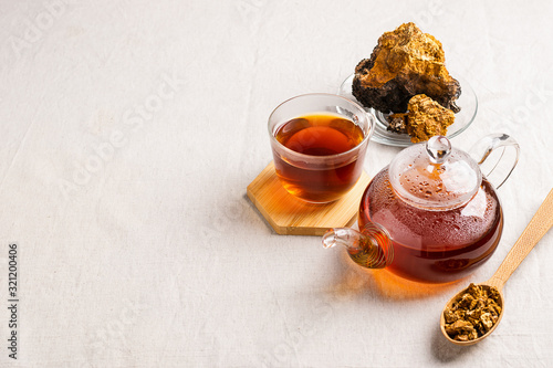 Wellness tea from chaga tree mushroom in a glass teapot and glass. Organic drink antioxidant gray natural background.