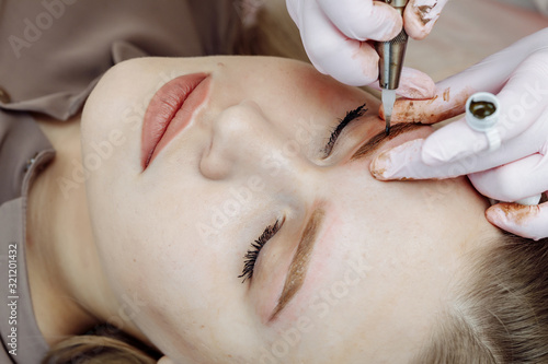 Permanent makeup, tattooing of eyebrows. Cosmetologist applying make up photo