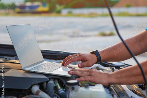 A man using laptop for auto diagnostics of a car engine.