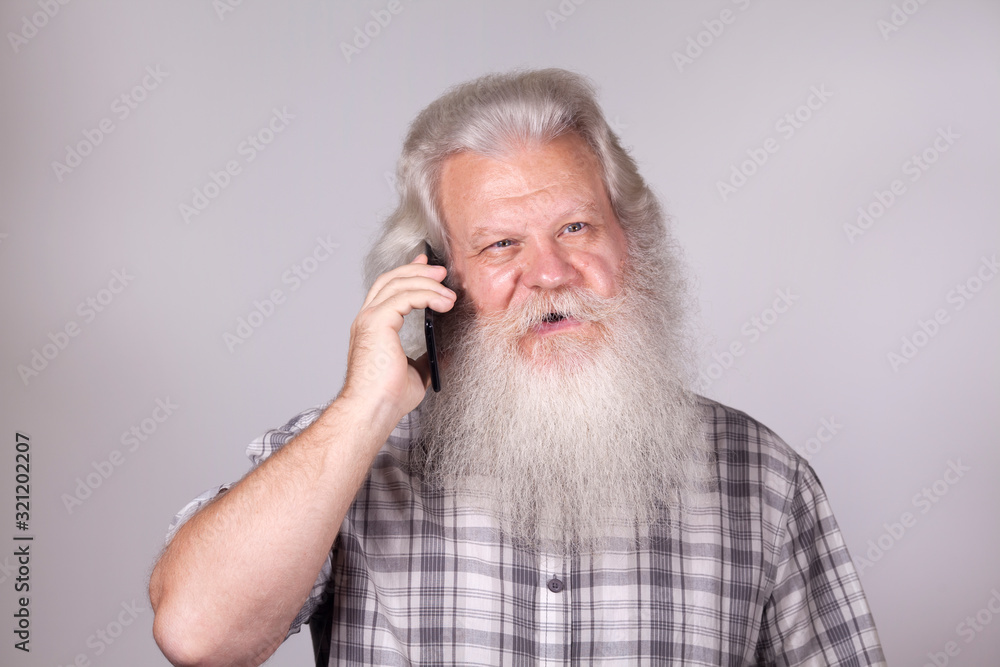 Senior thickset Caucasian happy man with splendid grey hair and beard on grey background, talking on sell phone. Attractive smile of elderly European handsome people close up. Beautiful macro portrait Senior thickset Caucasian happy man with splendid grey hair and beard on grey background, talking on sell phone. Attractive smile of elderly European handsome people close up. Beautiful macro portrait