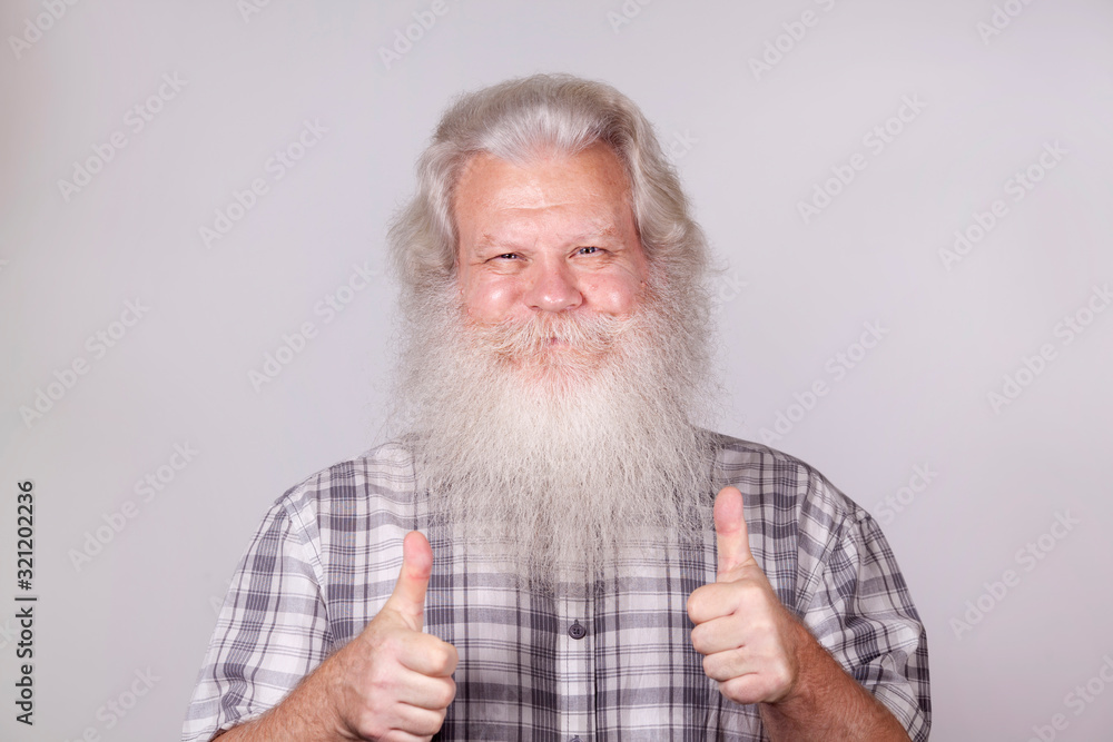 Senior thickset Caucasian happy man with splendid grey hair and beard on grey background with thumb up gesture. Attractive smile of elderly European handsome people close up. Beautiful macro portrait Senior thickset Caucasian happy man with splendid grey hair and beard on grey background with thumb up gesture. Attractive smile of elderly European handsome people close up. Beautiful macro portrait