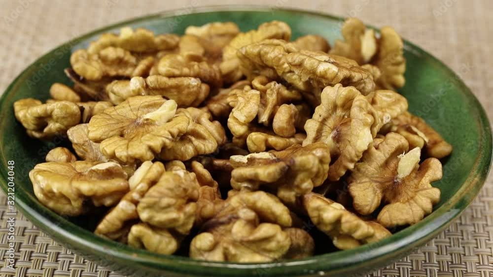 Female hands put peeled walnuts in a green plate, close-up Female hands put peeled walnuts in a green plate, close-up