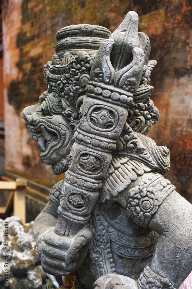 Ancient carved stone statue holds an ornate scepter outside a Hindu temple in Bali Indonesia