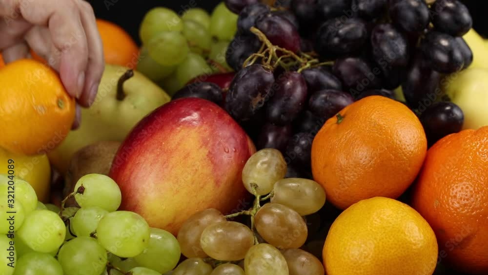 Female hand puts orange and mandarin on a large pile of different fruits Female hand puts orange and mandarin on a large pile of different fruits