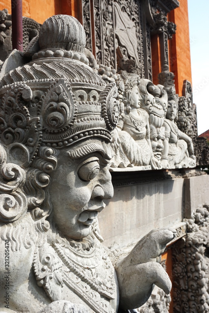Closeup of an ancient carved stone deity statue with more carvings behind at a Hindu temple in Bali Indonesia