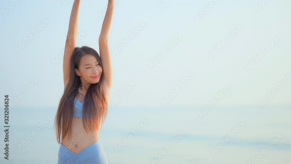 Beautiful Asian woman model standing in front of the sea looking aside interlock her fingers and raise hands up and spread arms over her head Beautiful Asian woman model standing in front of the sea looking aside interlock her fingers and raise hands up and spread arms over her head