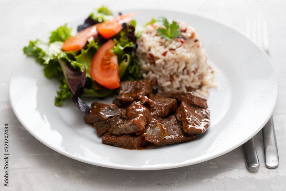 fried liver with salad and boiled rice on white plate